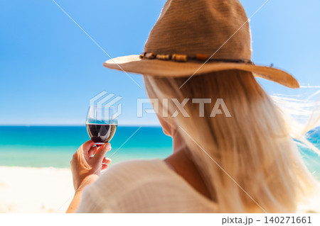 Woman relaxing with glass of red wine and turquoise sea view during sunny beach vacation in summer resort 140271661