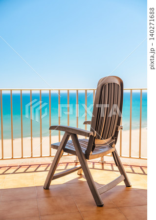 Empty chair on seaside balcony with panoramic ocean view and sunny tropical beach resort atmosphere Empty chair on seaside balcony with panoramic ocean view and sunny tropical beach resort atmosphere 140271688