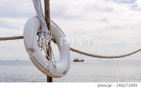White lifebuoy hanging on a wooden post and rope fence beside the Mediterranean Sea in Paphos, Cyprus. White lifebuoy hanging on a wooden post and rope fence beside the Mediterranean Sea in Paphos, Cyprus. 140271895