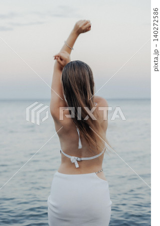 Woman stands by water, arms raised in celebration Woman stands by water, arms raised in celebration 140272586