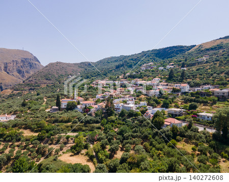 A picturesque Greek village with whitewashed houses nestled on a hill slope, overlooking a stunning mountain gorge in Crete, Greece. A perfect blend of traditional architecture and natural scenery 140272608
