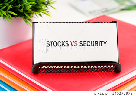 A striking comparison of stocks versus security rests on a stylish holder atop a stack of bright notebooks, framing a scene of financial insight and organization 140272978
