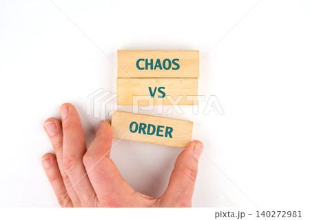 A hand reaches for wooden blocks displaying the words chaos and order, symbolizing a playful exploration of contrasting concepts in a thoughtful activity A hand reaches for wooden blocks displaying the words chaos and order, symbolizing a playful exploration of contrasting concepts in a thoughtful activity 140272981