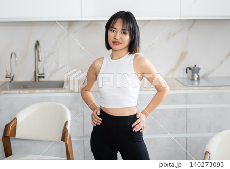 Smiling young Asian girl standing at table in the kitchen Smiling young Asian girl standing at table in the kitchen 140273093
