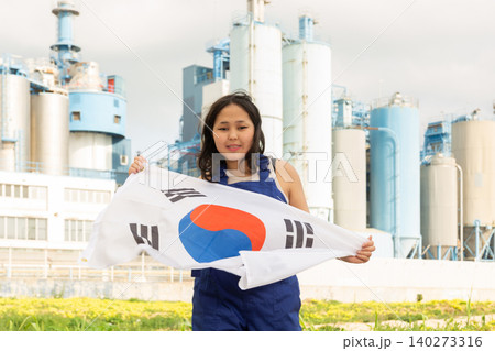 Happy asian girl in work clothes with flag of south korea standing in front of industrial scenery Happy asian girl in work clothes with flag of south korea standing in front of industrial scenery 140273316