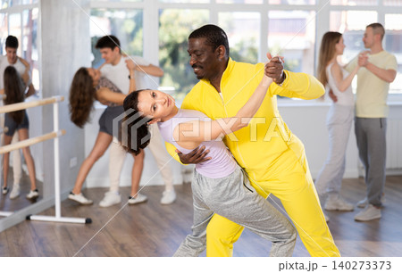 Smiling young woman wearing sportswear dancing in samba dance with african american partner during group class at dance salon 140273373