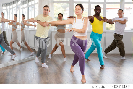 Smiling woman with multinational group active people enthusiastically training social latin cha-cha-cha dance movements in dance salon 140273385