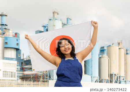 Happy young woman with flag of Japan against background of factory Happy young woman with flag of Japan against background of factory 140273422