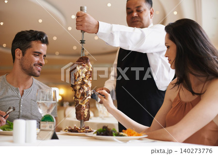 Couple, waiter and service for lunch in restaurant with meat, happiness and fine dining for anniversary or honeymoon. Man, woman and employee with steak on skewer, healthy meal and table in London 140273776