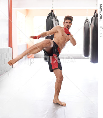 Fitness, gym and man with kickboxing for workout, strength and muscle exercise in sport. Male person, training and portrait with leg in air for energy, competition and challenge with punching bag Fitness, gym and man with kickboxing for workout, strength and muscle exercise in sport. Male person, training and portrait with leg in air for energy, competition and challenge with punching bag 140273899