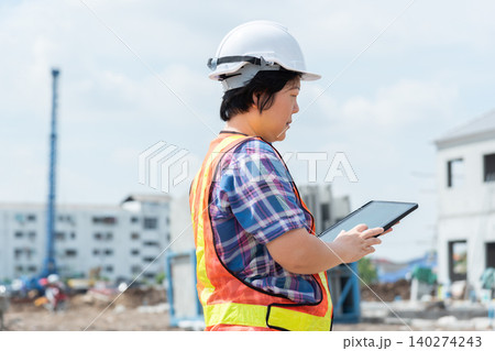 Construction engineer using digital tablet at building site wearing safety equipment monitoring project progress an active construction environment 140274243