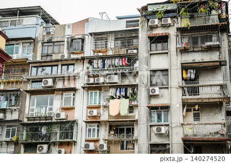 Dense residential buildings with drying laundry on balconies and air conditioners on old concrete apartment facades in Macau Dense residential buildings with drying laundry on balconies and air conditioners on old concrete apartment facades in Macau 140274520