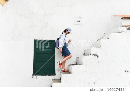 Mature 50 years old Russian woman tourist in cap walking down ancient concrete stairs near green window at Guia Lighthouse area in Macau destination Mature 50 years old Russian woman tourist in cap walking down ancient concrete stairs near green window at Guia Lighthouse area in Macau destination 140274584