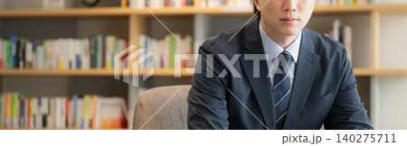 本棚の前で座る笑顔のハンサムな若い経営者や社長、ビジネスマンのポートレート 顔無しのバナー 本棚の前で座る笑顔のハンサムな若い経営者や社長、ビジネスマンのポートレート 顔無しのバナー 140275711