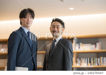 社長室のような本棚の前でパソコンを見ながら打ち合わせをする経営者、営業や上司と部下と笑顔カメラ目線 140276447