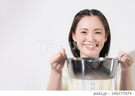 お鍋を手に持ちながら笑顔で紹介する若い女性のキッチンや料理のイメージ お鍋を手に持ちながら笑顔で紹介する若い女性のキッチンや料理のイメージ 140277074