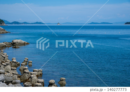 海岸に波消しブロック、遠くに小さい小島や島を望む波静かな海の風景 海岸に波消しブロック、遠くに小さい小島や島を望む波静かな海の風景 140277773