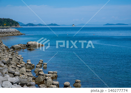 海岸に波消しブロック、遠くに小さい小島や島を望む波静かな海の風景 海岸に波消しブロック、遠くに小さい小島や島を望む波静かな海の風景 140277774