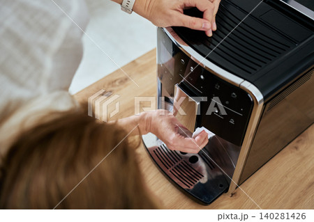Woman cleaning automatic coffee machine with cloth in kitchen Woman cleaning automatic coffee machine with cloth in kitchen 140281426