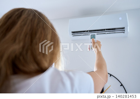 Woman adjusting air conditioner with remote control Woman adjusting air conditioner with remote control 140281453