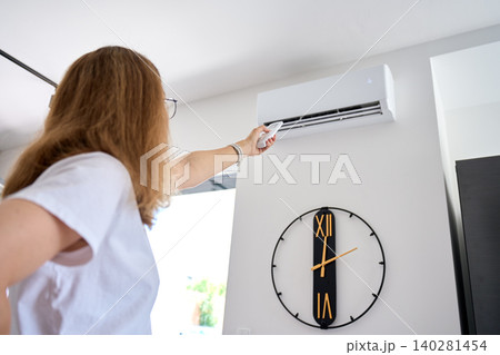 Woman adjusting air conditioner with remote control 140281454