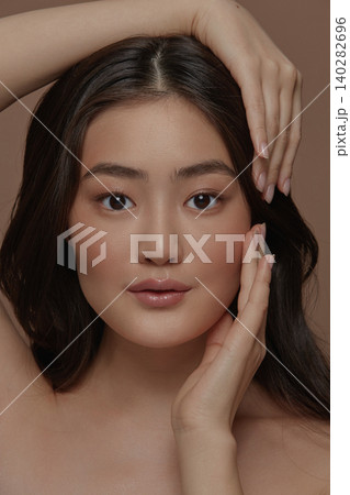 Beautiful portrait of an attractive japanese sensual young woman with a healthy clean skin and long brunette hair, touching her face standing isolated on a beige background Beautiful portrait of an attractive japanese sensual young woman with a healthy clean skin and long brunette hair, touching her face standing isolated on a beige background 140282696