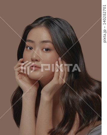 Beautiful portrait of an attractive japanese sensual young woman with a healthy clean skin and long brunette hair, touching her face standing isolated on a beige background 140282701