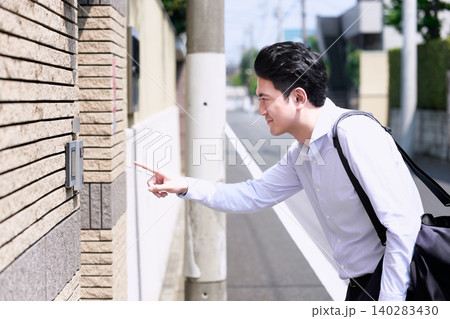 住宅街で住宅のインターフォンを指で押す30代の日本人の男性の営業職の会社員 住宅街で住宅のインターフォンを指で押す30代の日本人の男性の営業職の会社員 140283430