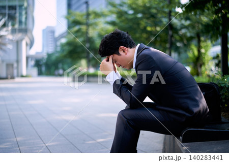 都会の屋外のベンチで仕事のストレスで頭を抱えて悩む20代の日本の男性の会社員 都会の屋外のベンチで仕事のストレスで頭を抱えて悩む20代の日本の男性の会社員 140283441