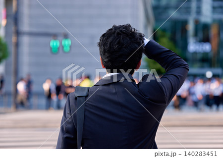 オフィス街で額に手を当てて風邪で体調の悪そうにしている30代の日本人のビジネスマンの男性の後ろ姿 オフィス街で額に手を当てて風邪で体調の悪そうにしている30代の日本人のビジネスマンの男性の後ろ姿 140283451