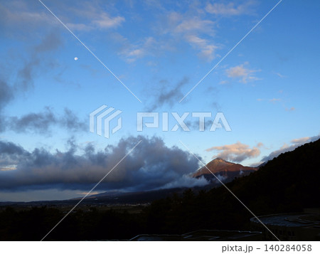 秋の早朝、霧が漂う青空に磐梯山に朝日が差しこむ。空には白い月が輝き、印象的で綺麗だ。 140284058