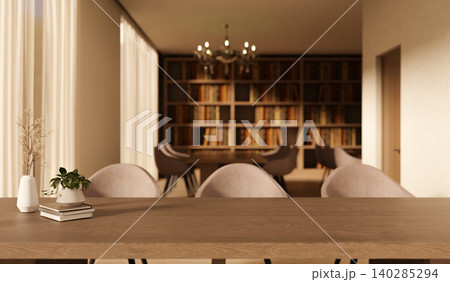 Wooden table with books and potted plant and chairs across bookshelf with chandelier in the library. 140285294