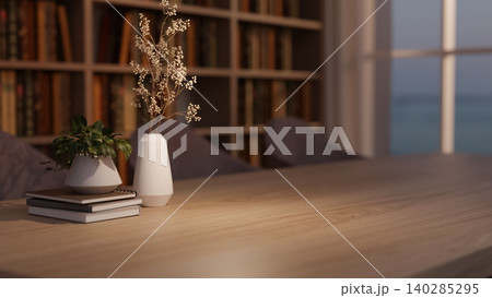 Wooden table with books, flower vase and potted plant across bookshelf and window in dim lit library Wooden table with books, flower vase and potted plant across bookshelf and window in dim lit library 140285295