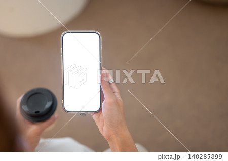 Close up of woman's hand holding coffee cup looking reading on white screen smartphone while sitting 140285899