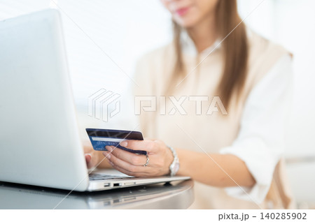 Close up of woman holding looking at credit card over laptop sitting at table in cafe or home office Close up of woman holding looking at credit card over laptop sitting at table in cafe or home office 140285902