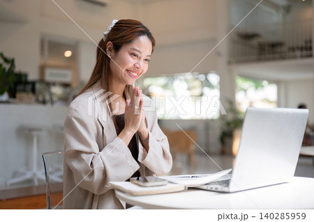 Happy asian woman clapping hands and looking at laptop with a smile while sitting at table in cafe Happy asian woman clapping hands and looking at laptop with a smile while sitting at table in cafe 140285959