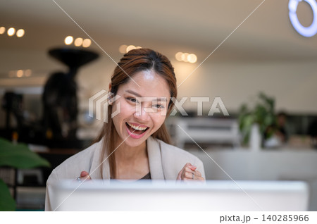 Excited mature asian woman looking at a laptop and making a fist while sitting at table in the cafe. Excited mature asian woman looking at a laptop and making a fist while sitting at table in the cafe. 140285966