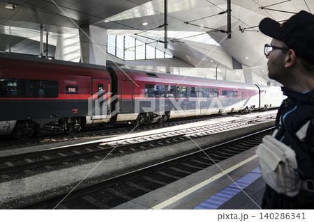 Person waiting for a train on a platform at a modern railway station, featuring sleek and contemporary architecture Person waiting for a train on a platform at a modern railway station, featuring sleek and contemporary architecture 140286341