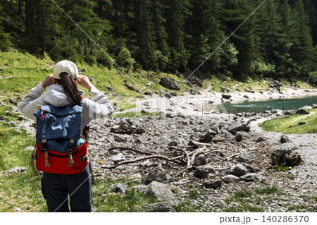 Traveler with backpack looking at mountain lake in the Austrian Alps, highlighting exploring remote mountain landscapes 140286370