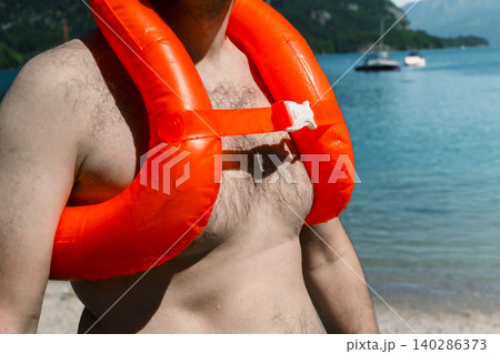 Orange inflatable life vest worn by a man standing on a lake shore, highlighting adventure travel with proper safety gear Orange inflatable life vest worn by a man standing on a lake shore, highlighting adventure travel with proper safety gear 140286373