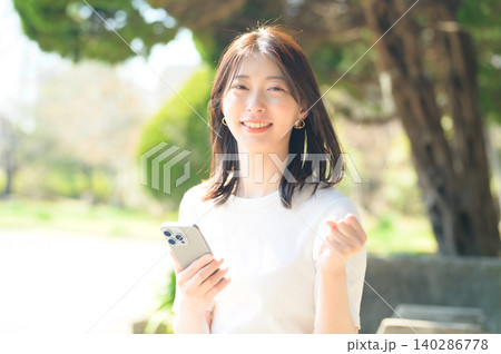公園でスマートフォンを持って喜ぶ日本人女性 公園でスマートフォンを持って喜ぶ日本人女性 140286778