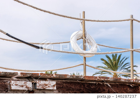 White lifebuoy on a rope fence by Mediterranean seaside in Paphos, Cyprus. Minimal resort setting with cloudy sky, palm tree. White lifebuoy on a rope fence by Mediterranean seaside in Paphos, Cyprus. Minimal resort setting with cloudy sky, palm tree. 140287237