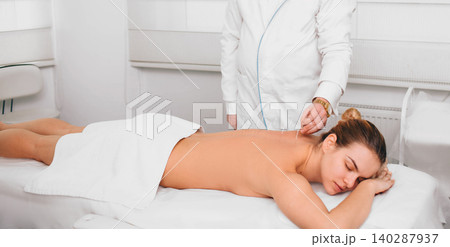Acupuncturist inserting a needle into a female back. patient having traditional Chinese treatment using needles to restore an energy flow through specific points on the skin. Acupuncturist inserting a needle into a female back. patient having traditional Chinese treatment using needles to restore an energy flow through specific points on the skin. 140287937