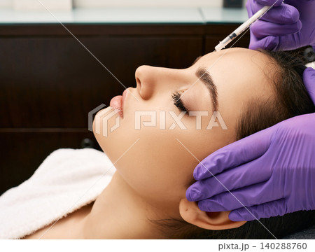 Botulinum toxin injections to beautiful woman's forehead, side view. Anti-aging procedure after 30 years, cosmetologist doing beauty injection Botulinum toxin injections to beautiful woman's forehead, side view. Anti-aging procedure after 30 years, cosmetologist doing beauty injection 140288760