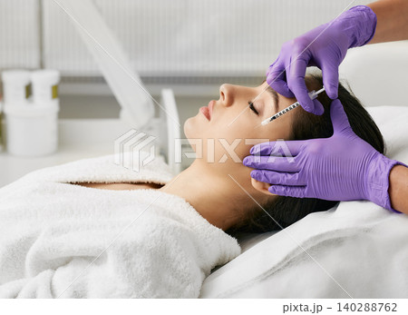 Beautiful woman during facial mesotherapy. Beautician doing anti-aging injection for tightening skin and remove eye wrinkles Beautiful woman during facial mesotherapy. Beautician doing anti-aging injection for tightening skin and remove eye wrinkles 140288762