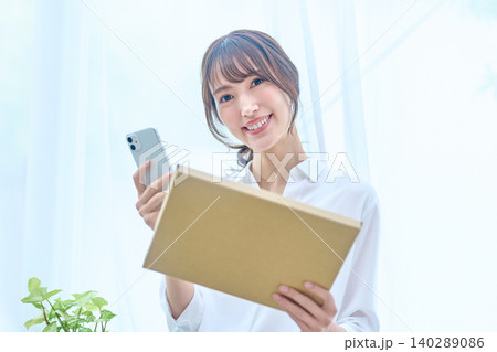 荷物とスマホを手にこちらを見て微笑む白シャツの女性 荷物とスマホを手にこちらを見て微笑む白シャツの女性 140289086