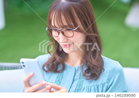 屋外でメガネをかけてスマホを見る若い女性 140289090