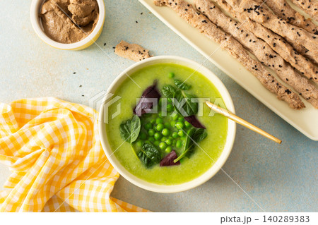 A bowl of creamy broccoli and green pea soup sits on a green plate. Next to it is liver pate in a small dish and grissini on a white platter. This meal provides healthy options A bowl of creamy broccoli and green pea soup sits on a green plate. Next to it is liver pate in a small dish and grissini on a white platter. This meal provides healthy options 140289383