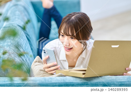 スマホとノートパソコンで通販を楽しむソファの女性 140289393