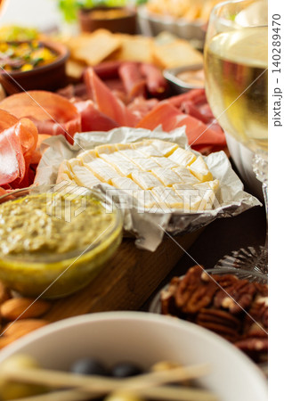 Gathered around a beautifully arranged charcuterie board filled with assorted cheeses, delicious sausages, creamy hummus, and fresh grapes. Perfect for a small gathering Gathered around a beautifully arranged charcuterie board filled with assorted cheeses, delicious sausages, creamy hummus, and fresh grapes. Perfect for a small gathering 140289470